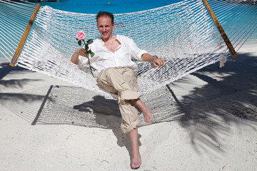 The happy man with a rose in hands in a hammock, on a background the sea.