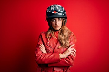 Young beautiful brunette motrocyclist woman wearing moto helmet over red background skeptic and nervous, disapproving expression on face with crossed arms. Negative person.