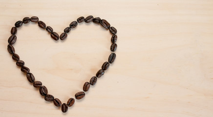The shape of the heart is laid out on a light background of roasted coffee beans, there is room for text.