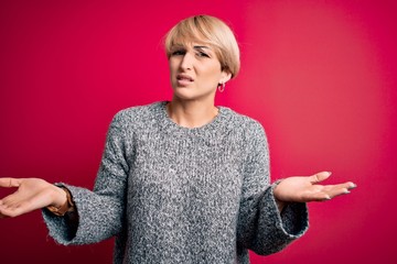 Young blonde woman with modern short hair wearing casual sweater over pink background clueless and...