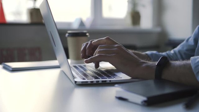 Closeup of man hands typing at laptop in the business workplace. Spbd electonic apple watch on male hand. concept studying, digital, millennial. hipster guy freelancer at cafe with coffee cup
