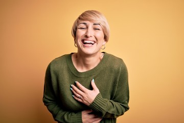 Young blonde woman with modern short hair wearing casual sweater over yellow background smiling and...