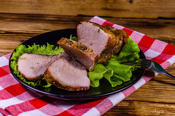 Slices of baked pork meat and lettuce leaves on a black plate