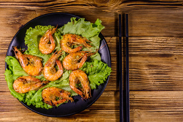 Plate with grilled shrimps, lettuce leaves and chopsticks on a wooden table. Top view