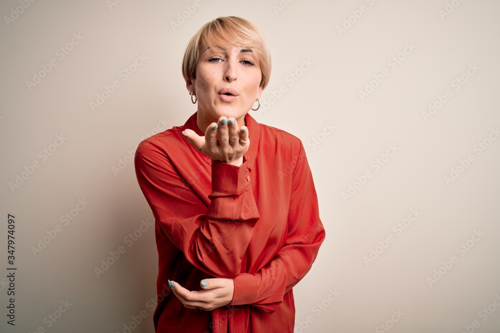 Sticker Young beautiful business blonde woman with short hair standing over isolated background looking at the camera blowing a kiss with hand on air being lovely and sexy. Love expression.