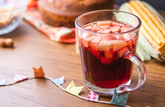 Hot mulled wine from Brazil with apple pieces, tipical in Festa Junina Festival. Traditional food of Brazil, June Partys sweet. Rustic Wood Background with peanuts and brazilian candy. Top View