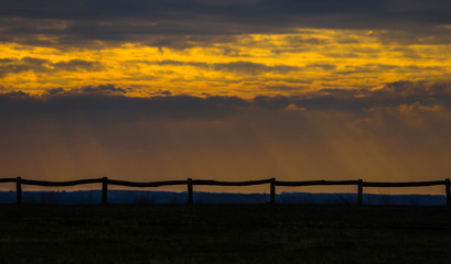 Sunset on a cloudy day with a wooden fence in the foreground.