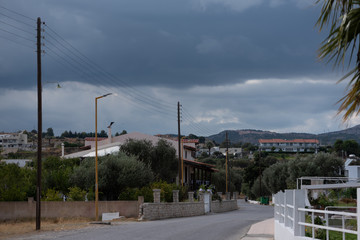 Fototapeta na wymiar Thunder clouds over the town in Greece. Street before the rain in summer.
