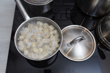 Ravioli in pan, boiling water, silver metal background. Cooking Pelmeni, russian dumplings stuffed with minced meat, in steel stewpot on ceramic stove in home kitchen. Varenyky, vareniki.