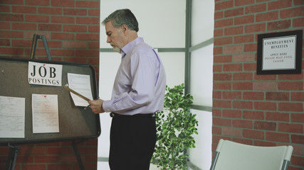 A mature man recently unemployed holding an employment application waits in the unemployment office looking over some job postings.