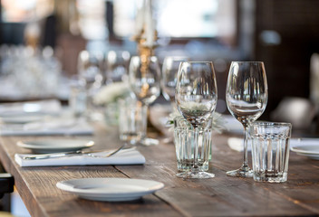 Glasses, flowers, fork, knife served for dinner in restaurant with cozy interior, retro film filter effect	