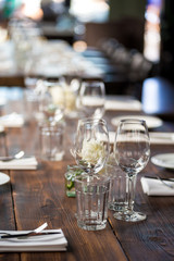 Glasses, flowers, fork, knife served for dinner in restaurant with cozy interior, retro film filter effect	