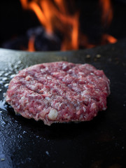 Close up of one single burger pattie on a fire plate.