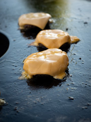 Three burger patties with molten cheese on a fire plate.