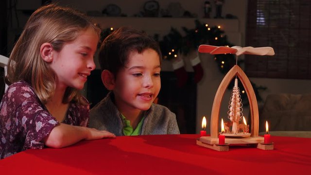 Two young siblings share the magic of the holidays watching a traditional, hand-carved Christmas pyramid turn.