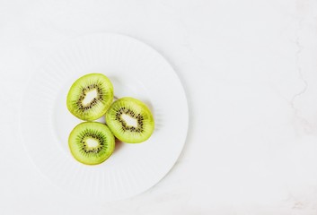 Three halves of ripe kiwi on a white marble background. Top view, copy space