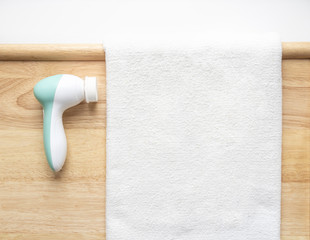 Device massager brush for cleaning the skin of the face with a nozzle-sponge on a wooden background next to a white towel. Personal care at home.