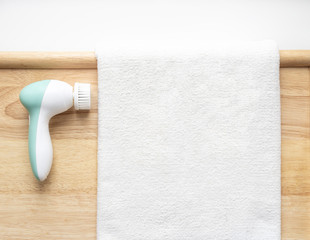 Massager brush for cleaning the skin of the face with a brush head on a wooden background next to a white towel. Personal care at home.