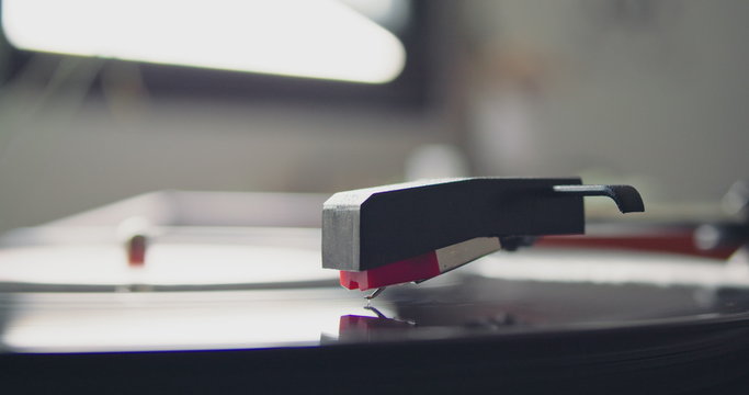 Closeup of portable vintage headshell of record player going down playing on vynil record on blurred background