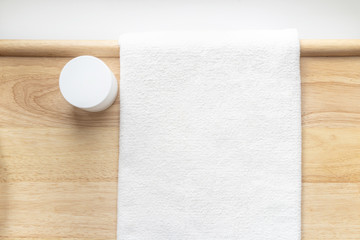 White jar of face cream on a wooden background next to a white towel.
