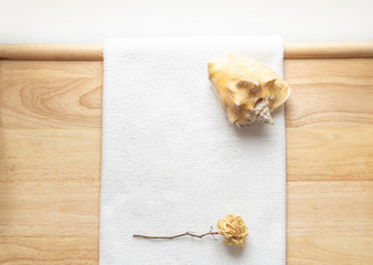 Huge natural seashell on a white towel on a wooden background and dry flower of rose