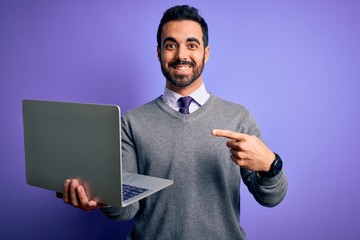Young handsome businessman with beard working using laptop over purple background very happy pointing with hand and finger