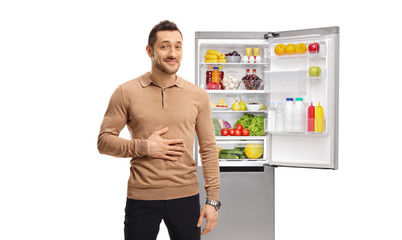 Man holding his hand on his stomach and standing in front of a full refrigerator