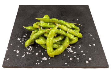 Tasty steamed edamame on a black stone plate, isolated on white background