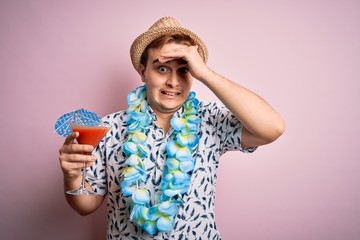 Young redhead tourist man on vacation wearing hat and hawaiian lei drinking cocktail stressed and frustrated with hand on head, surprised and angry face