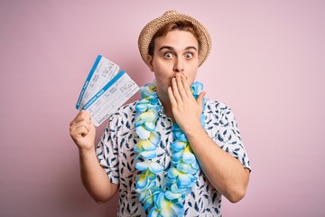 Handsome redhead tourist man on vacation wearing hawaiian lei holding boarding pass airlane covering mouth with hand, shocked and afraid for mistake. Surprised expression