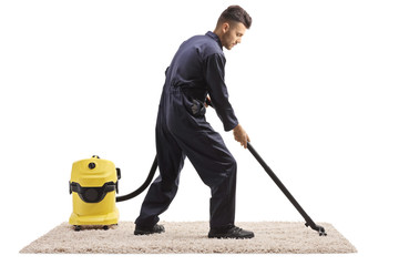 Male worker in a uniform with a vacuum cleaner hoovering a carpet