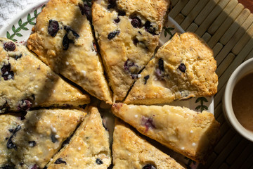 Blueberry scones cut in triangles on a round plate with a cup of hot drink. 