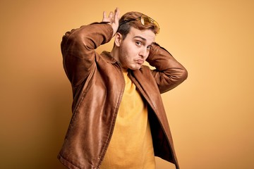 Young handsome redhead man wearing casual leather jacket over isolated yellow background Doing bunny ears gesture with hands palms looking cynical and skeptical. Easter rabbit concept.