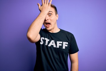 Naklejka premium Young handsome redhead worker man wearing staff t-shirt uniform over purple background surprised with hand on head for mistake, remember error. Forgot, bad memory concept.