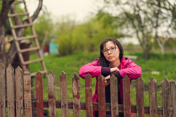 pensive woman stands near an old wooden fence