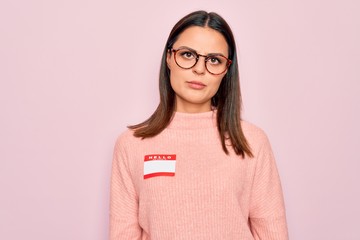 Young beautiful brunette woman wearing sticker with hello my name is message thinking attitude and sober expression looking self confident