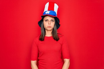 Young beautiful brunette woman wearing united states hat celebrating independence day puffing cheeks with funny face. Mouth inflated with air, crazy expression.