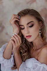 Fototapeta premium A beautiful girl with natural, beautiful, professional makeup and a fancy fashion fashion cut in her hair and long white pearl earrings. hands near the face, a large portrait. selective focus