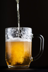 bright and fresh beer is poured into a large glass goblet. Selective focus macro shot with shallow depth of field isolated on black background