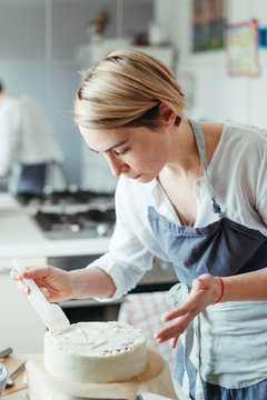 A Middle Aged Woman Pastry Chef Or Baker Prepares A Cake And Decorates It With Icing.