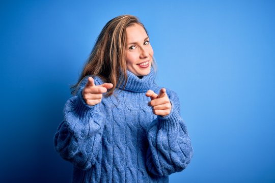 Young beautiful blonde woman wearing casual turtleneck sweater over blue background pointing fingers to camera with happy and funny face. Good energy and vibes.