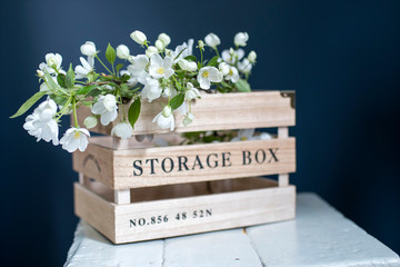 Wooden box for storing things with the inscription Sweet home with an apple flowering branch on a white vintage stool against a dark blue wall.