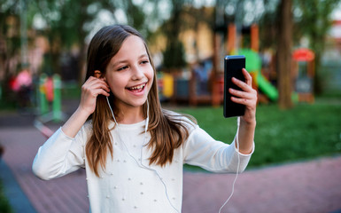 Childhood time. Cute little girl listening to music with mobile phone and headphones. Lifestyle...