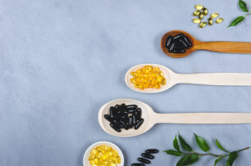 Black pill, yellow pill and wooden spoon on grey background