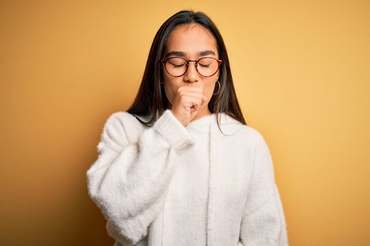 Young beautiful asian woman wearing casual sweater and glasses over yellow background feeling unwell and coughing as symptom for cold or bronchitis. Health care concept.
