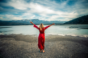 Beautiful woman with arms raised travel on a mountain lake. Girl power concept.