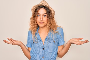 Young beautiful woman with blue eyes wearing casual denim dress and summer hat clueless and...