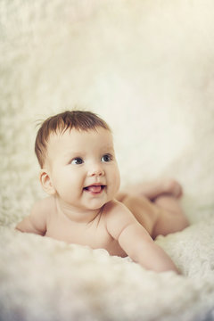 Happy young baby lying on tummy on a light bedspread.