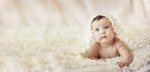 Happy young baby lying on tummy on a light bedspread. © Chendekova Liudmila