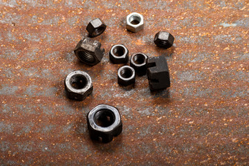 Tuercas de diferentes tamaños sobre una lamina metalica oxidada.